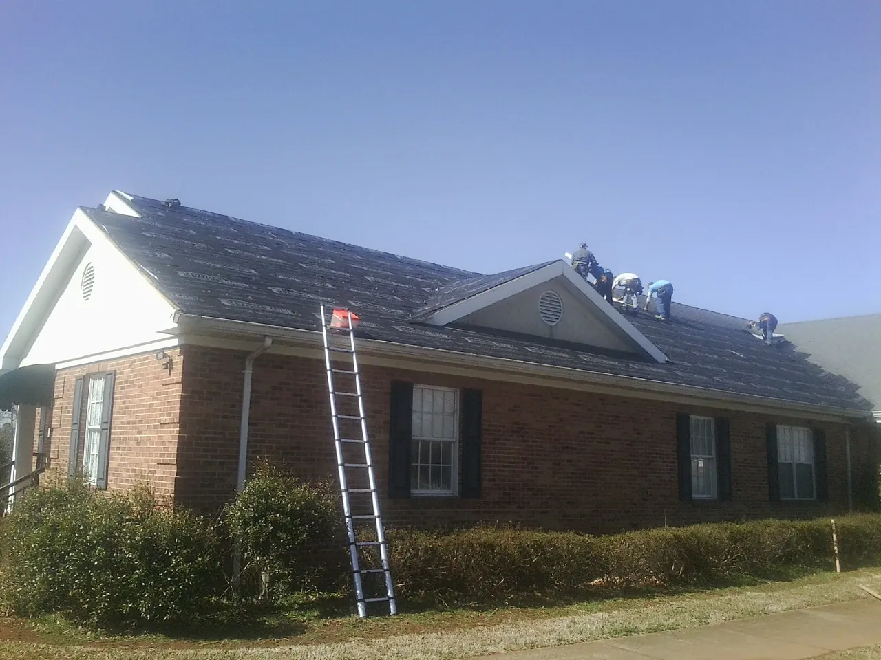 Crew tearing shingles off a brick ranch roof with a ladder set — Emergency Roof Repair work by our crew in South Sioux City