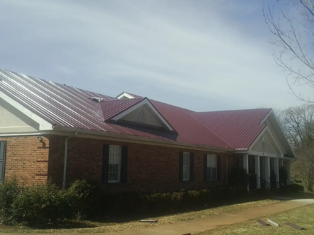 Red metal roof with gabled entries on a long brick building, from a Hail Damage Roof Repair job in South Sioux City