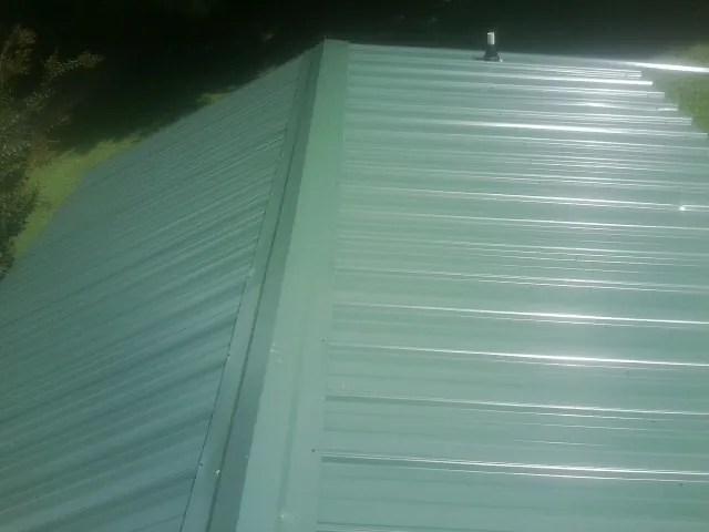 New green metal panels meeting at the ridge of a roof — Flat Roof Repair work by our crew in South Sioux City