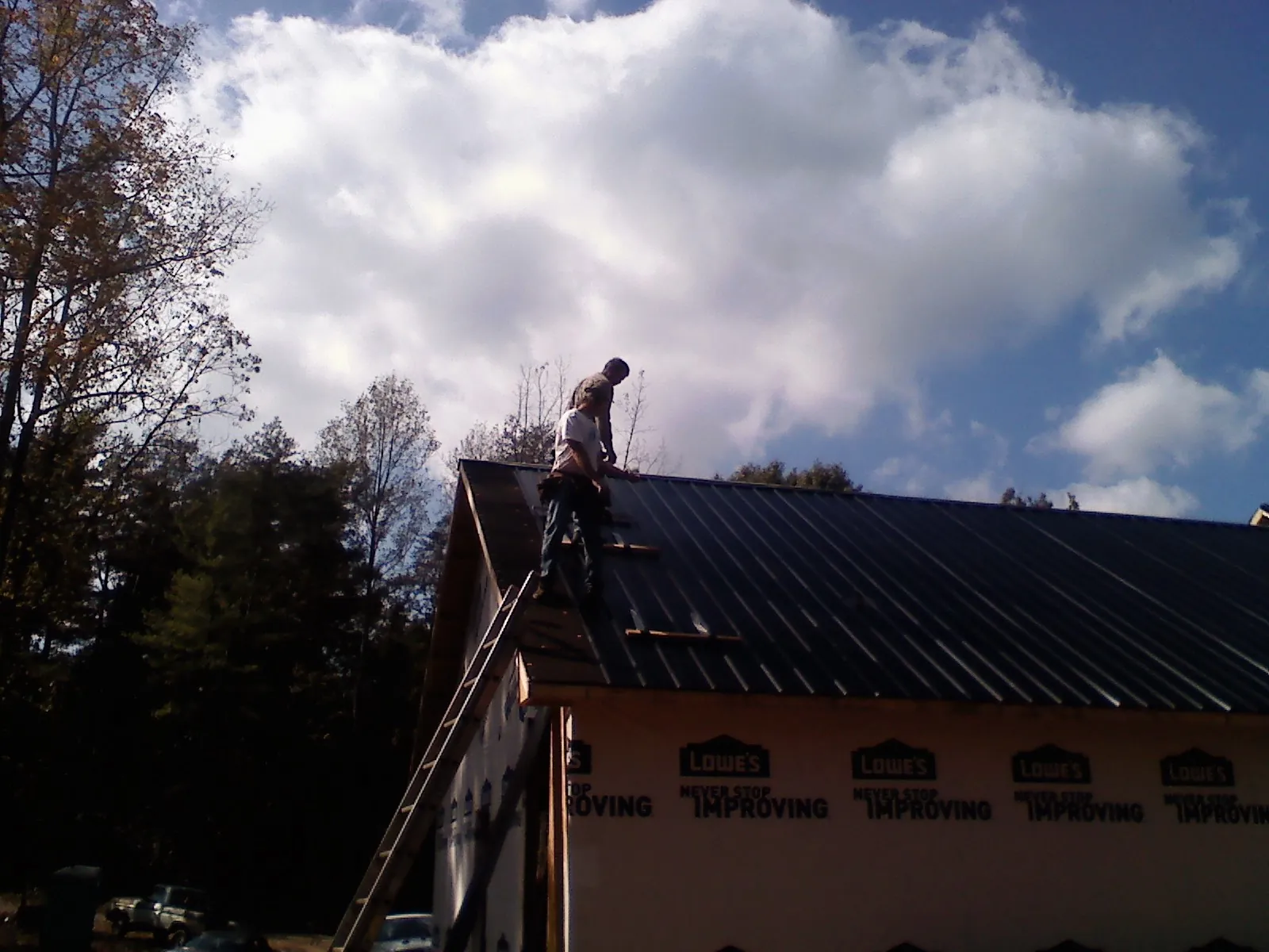 Roofer fastening dark metal panels high against a cloudy sky, from a Roof Inspection job in South Sioux City
