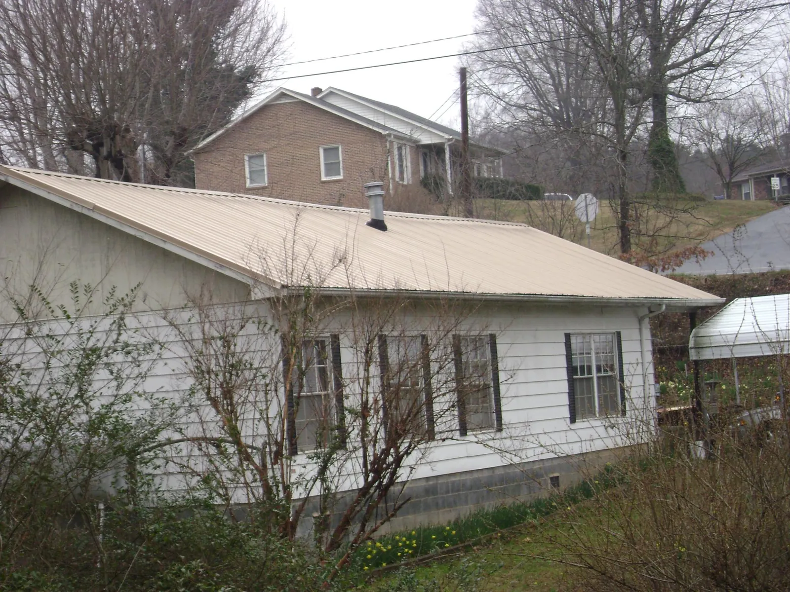 Tan metal roof on a white sided house set into a hillside — Commercial Roofing by Roofing Brothers in South Sioux City